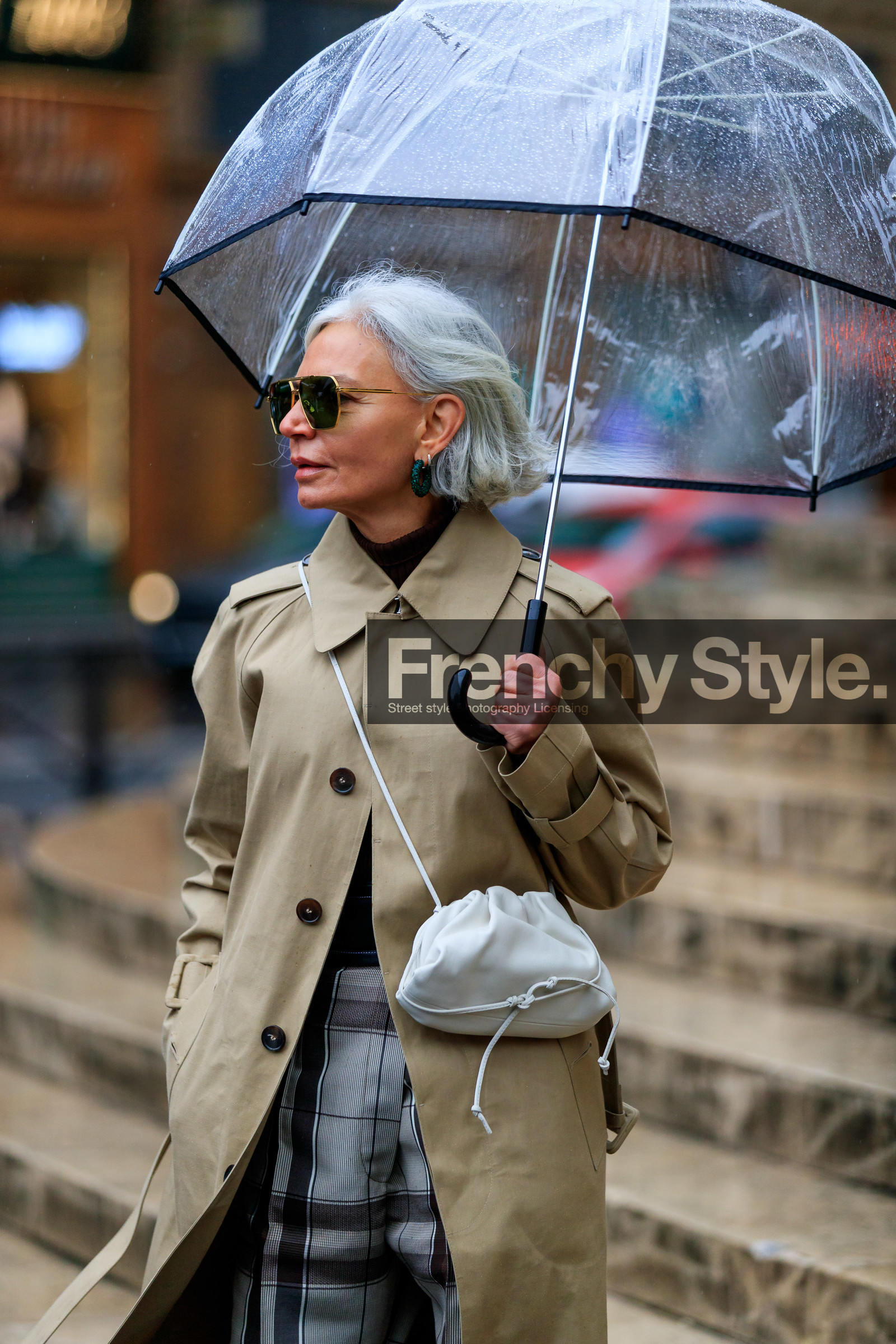 beige trench coat, light beige leather bag, crossbody bag, metalic frame sunglasses, aviator sunglasses, geometric shape glasses, bottega veneta bag, bottega veneta sunglasses, green earrings, hoop earrings, strassed earrings, grey pants, checked pants, brown pants, plaid pants, sheer umbrella, fashion week, frenchystyle, FW, jonathan paciullo, street style, PFW, PARIS, vertical, atmosphere details, detail