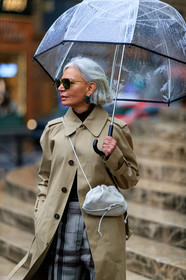 beige trench coat, light beige leather bag, crossbody bag, metalic frame sunglasses, aviator sunglasses, geometric shape glasses, bottega veneta bag, bottega veneta sunglasses, green earrings, hoop earrings, strassed earrings, grey pants, checked pants, brown pants, plaid pants, sheer umbrella, fashion week, frenchystyle, FW, jonathan paciullo, street style, PFW, PARIS, vertical, atmosphere details, detail